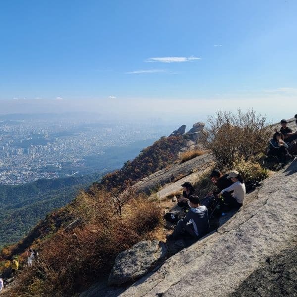 How To Hike Bukhansan Baegundae Peak: Seoul's Best Hike 2024 6 People sitting on Baegundae Peak looking at Seoul